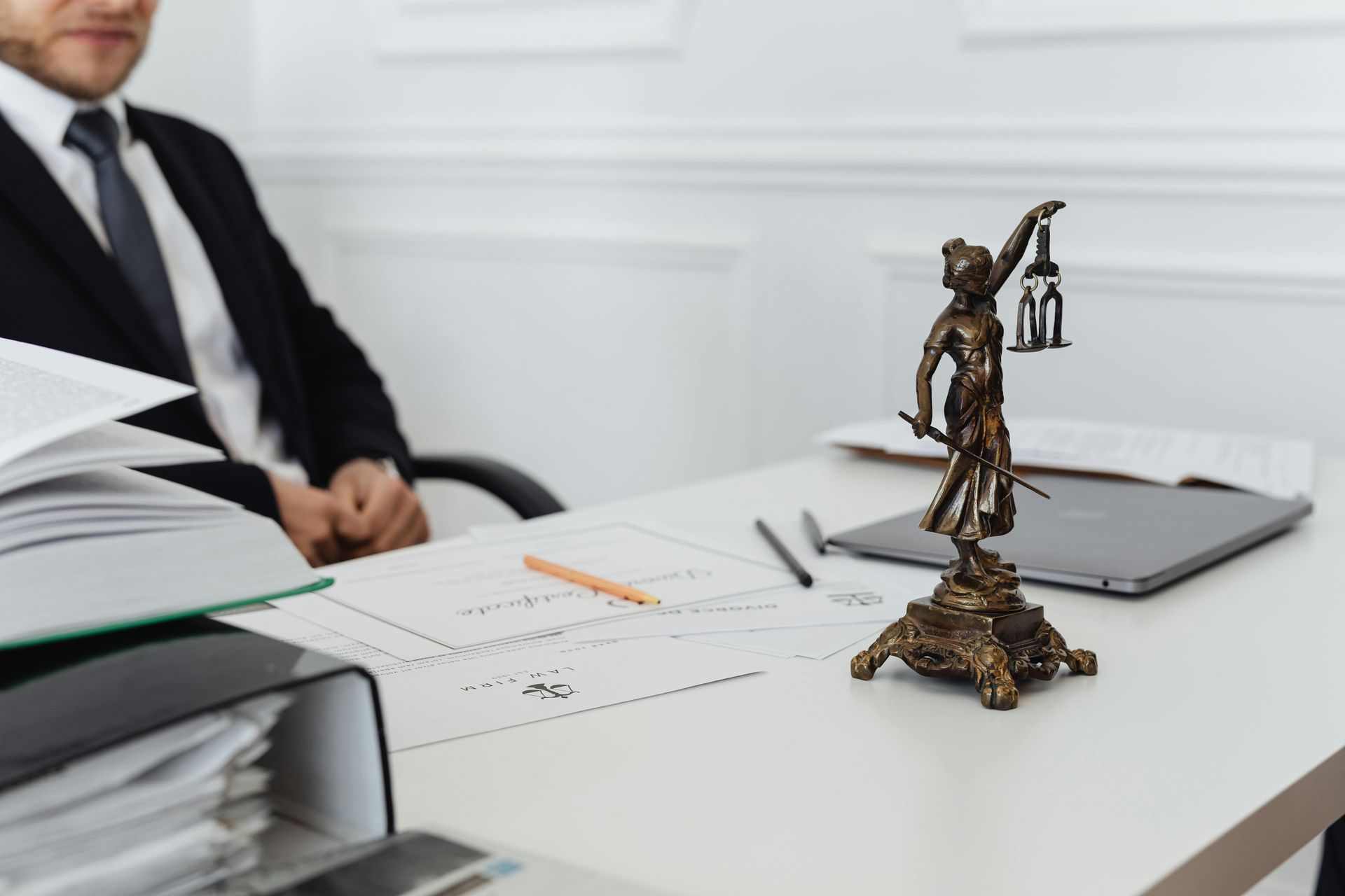Un avocat à son bureau, avec des documents juridiques, une statue de la Justice et un ordinateur portable.