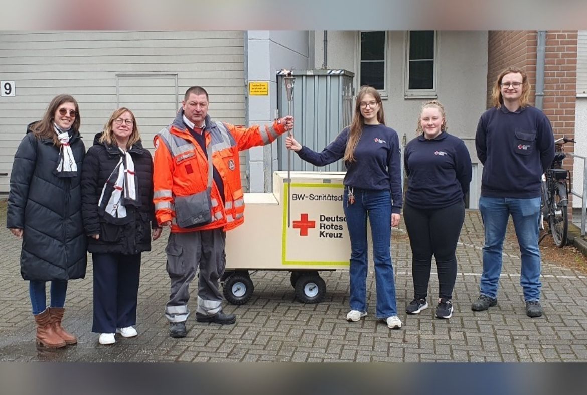 Eine Gruppe von Menschen steht neben einem Wagen mit einem roten Kreuz darauf.