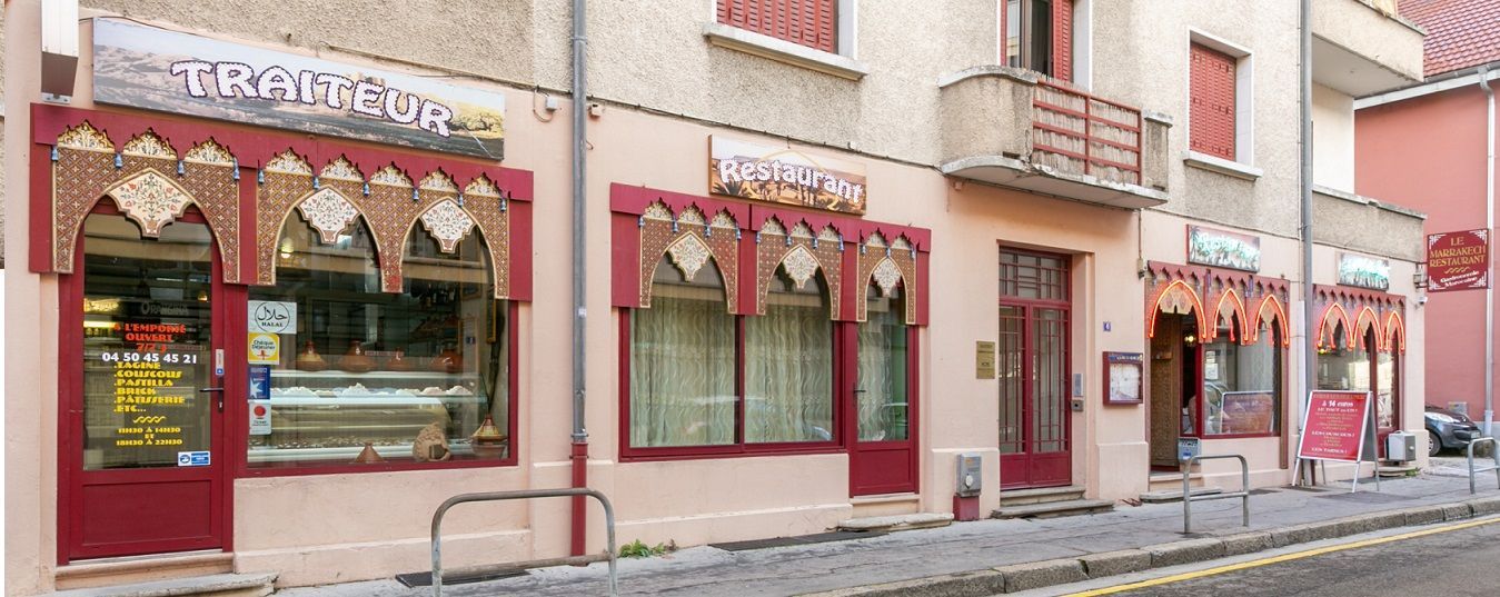 Vue depuis la rue d'une façade rose avec des auvents rouges et de grandes fenêtres le long d'une rue pavée étroite.