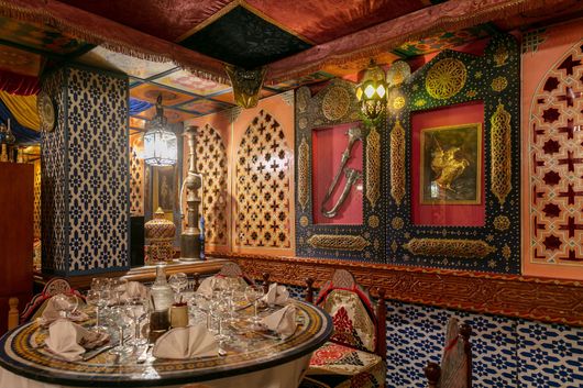 Salle à manger opulente avec murs à motifs, lampes ornementées et table dressée avec argenterie et verrerie.