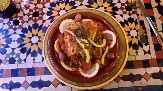 Plat servi dans une assiette avec des tranches de citron, sur une table aux motifs colorés.
