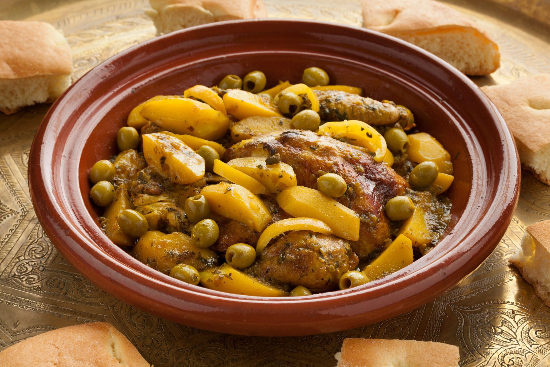 Bol en terre cuite contenant du poulet rôti et des quartiers de pommes de terre avec des olives, sur une table rustique