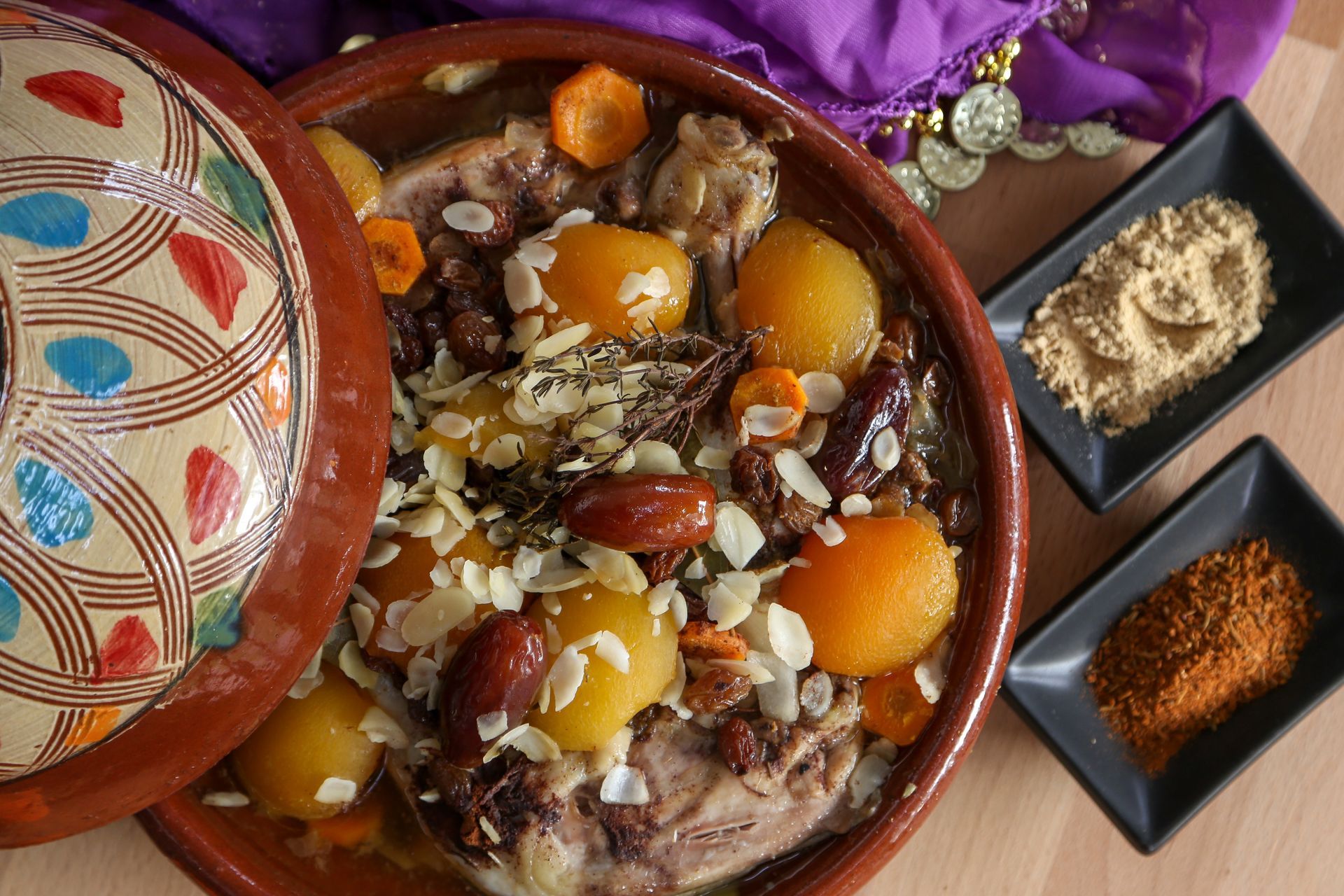 Bol décoratif de couscous marocain aux pois chiches et aux abricots, à côté de plats à épices et d'un tissu violet