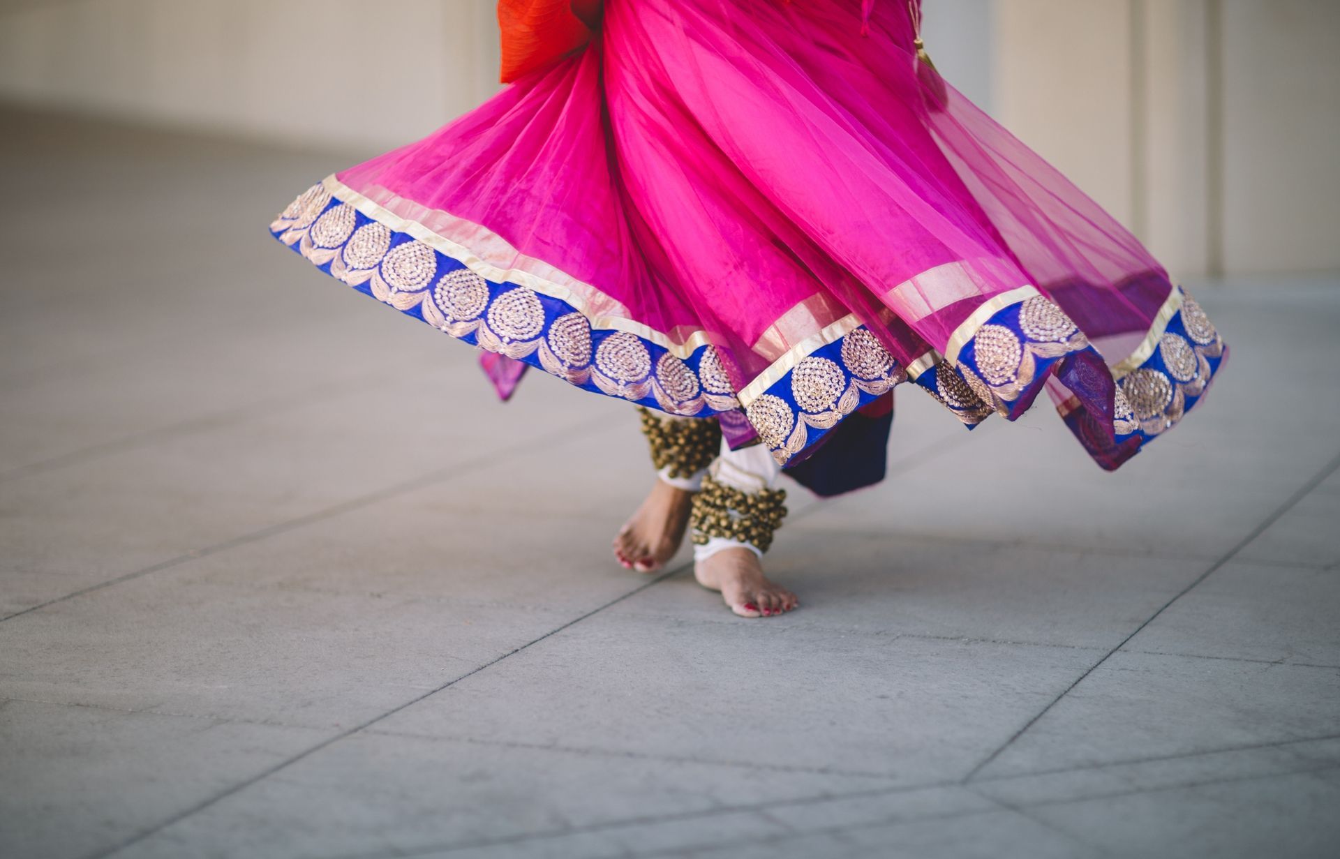 Une jupe rose brodée tournoie tandis qu'une personne danse pieds nus sur un sol carrelé.