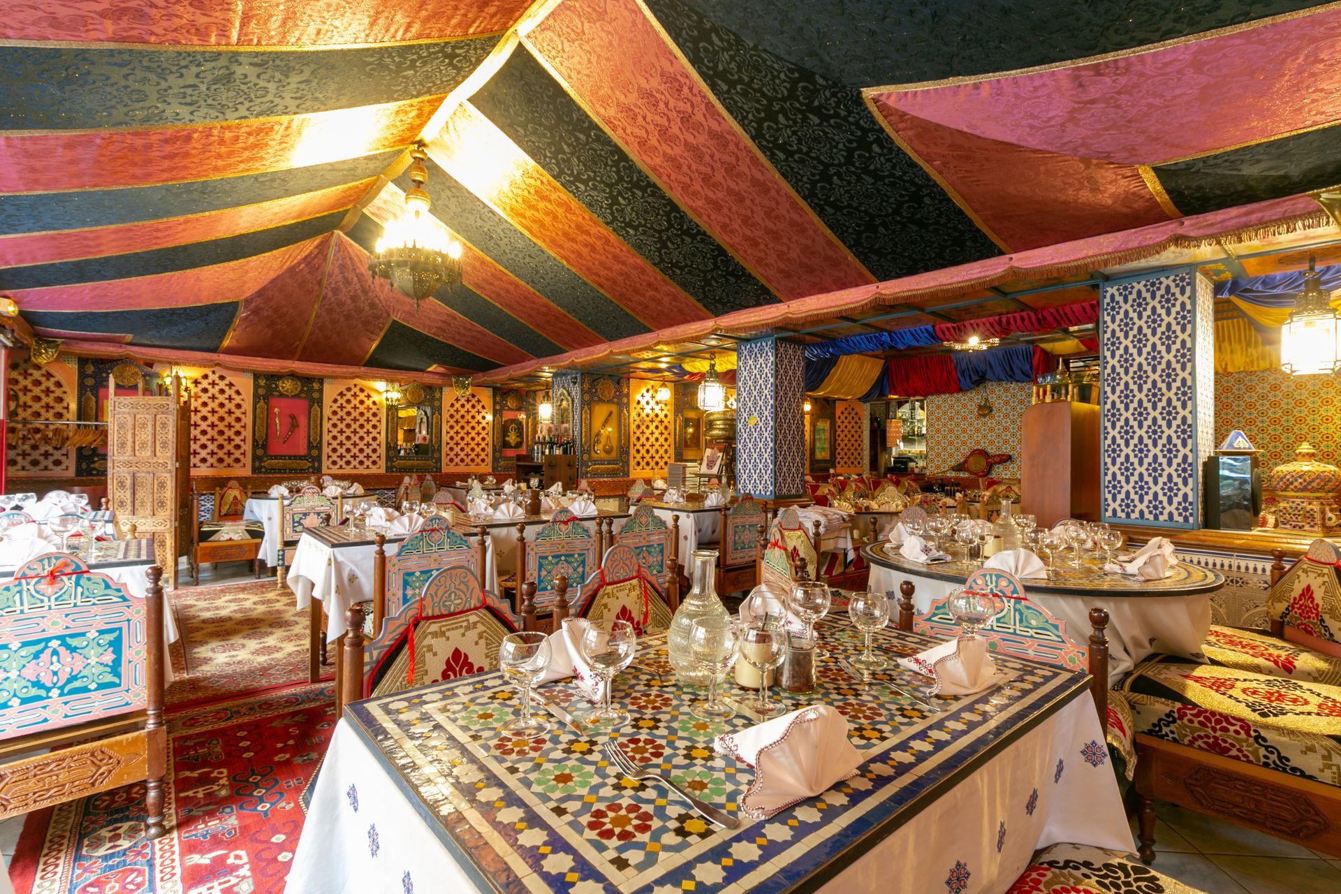 Intérieur coloré d'un restaurant sous une tente, avec des tables et des chaises à motifs et un éclairage chaleureux.