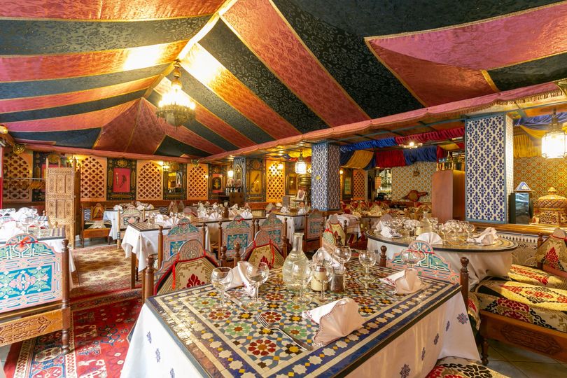 Salle à manger sous une tente décorée avec des rideaux colorés, des tables à motifs et un éclairage chaleureux aux lanternes