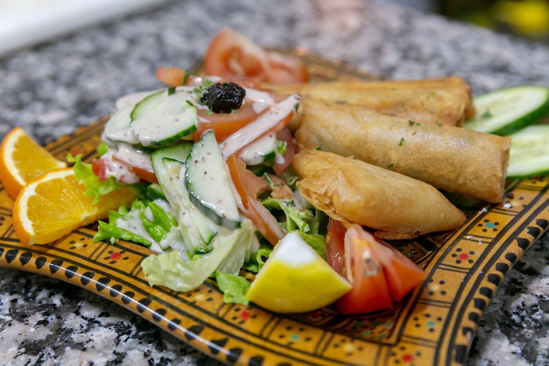 Salade avec des bricks frits, concombre, tomate et tranches d'orange sur une assiette à motifs