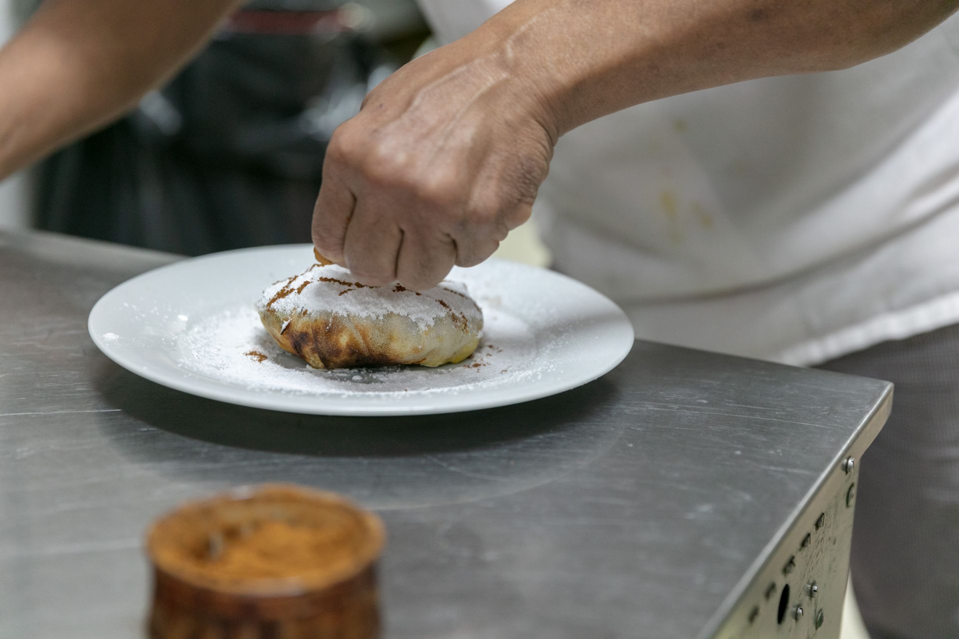 Une main dépose la garniture sur une assiette dressée sur un comptoir en acier inoxydable