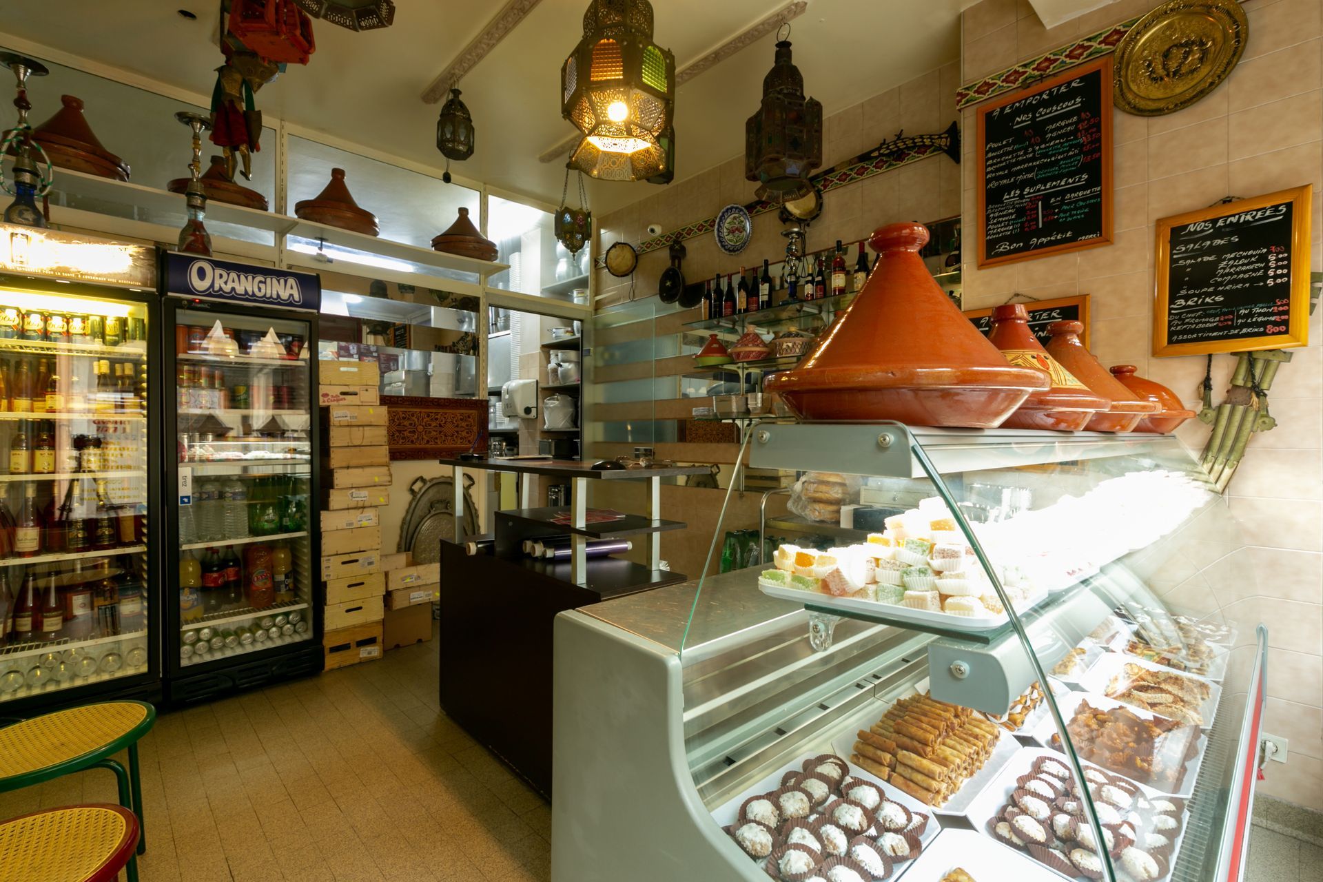 Intérieur chaleureux du restaurant avec des vitrines à pâtisseries, étagères et lampes suspendues