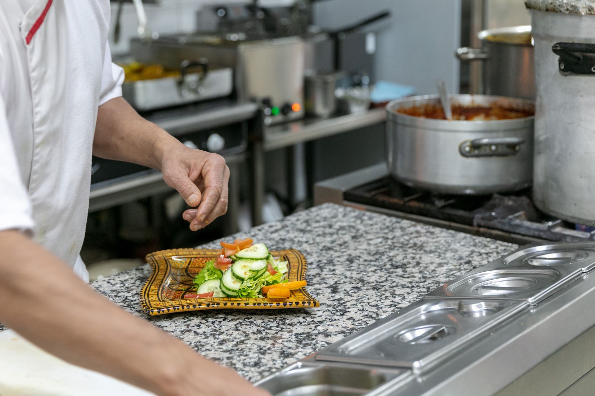 Un chef dresse une assiette de légumes près d'une plaque de cuisson dans une cuisine professionnelle.