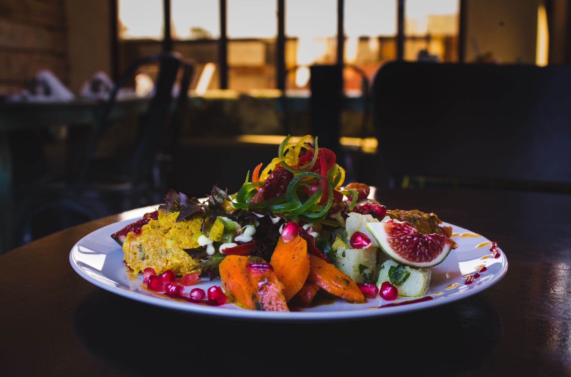 Salade composée raffinée de figues, de baies et de verdure, présentée sur une table sombre près d'une fenêtre.