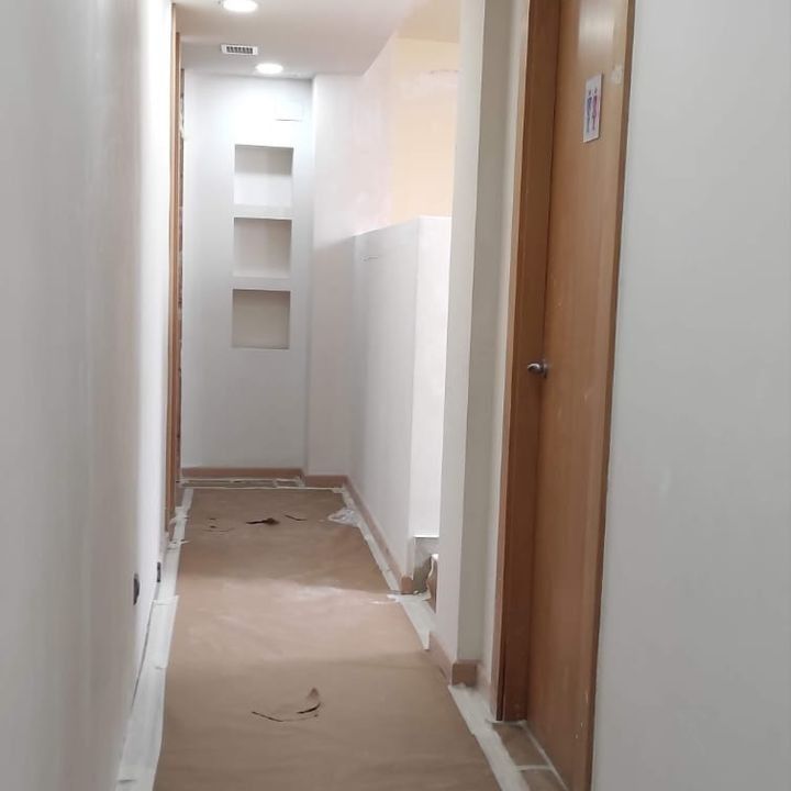 Un largo pasillo con una puerta de madera y estantes en la pared.