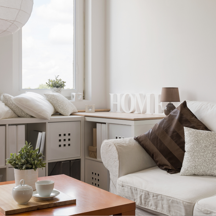 Acogedora sala de estar con sofá blanco, mesa de madera y almohadas decorativas junto a una ventana.