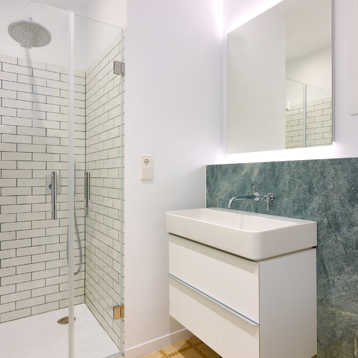 Baño moderno con tocador blanco, pared con detalles de mármol verde y ducha con azulejos de metro.
