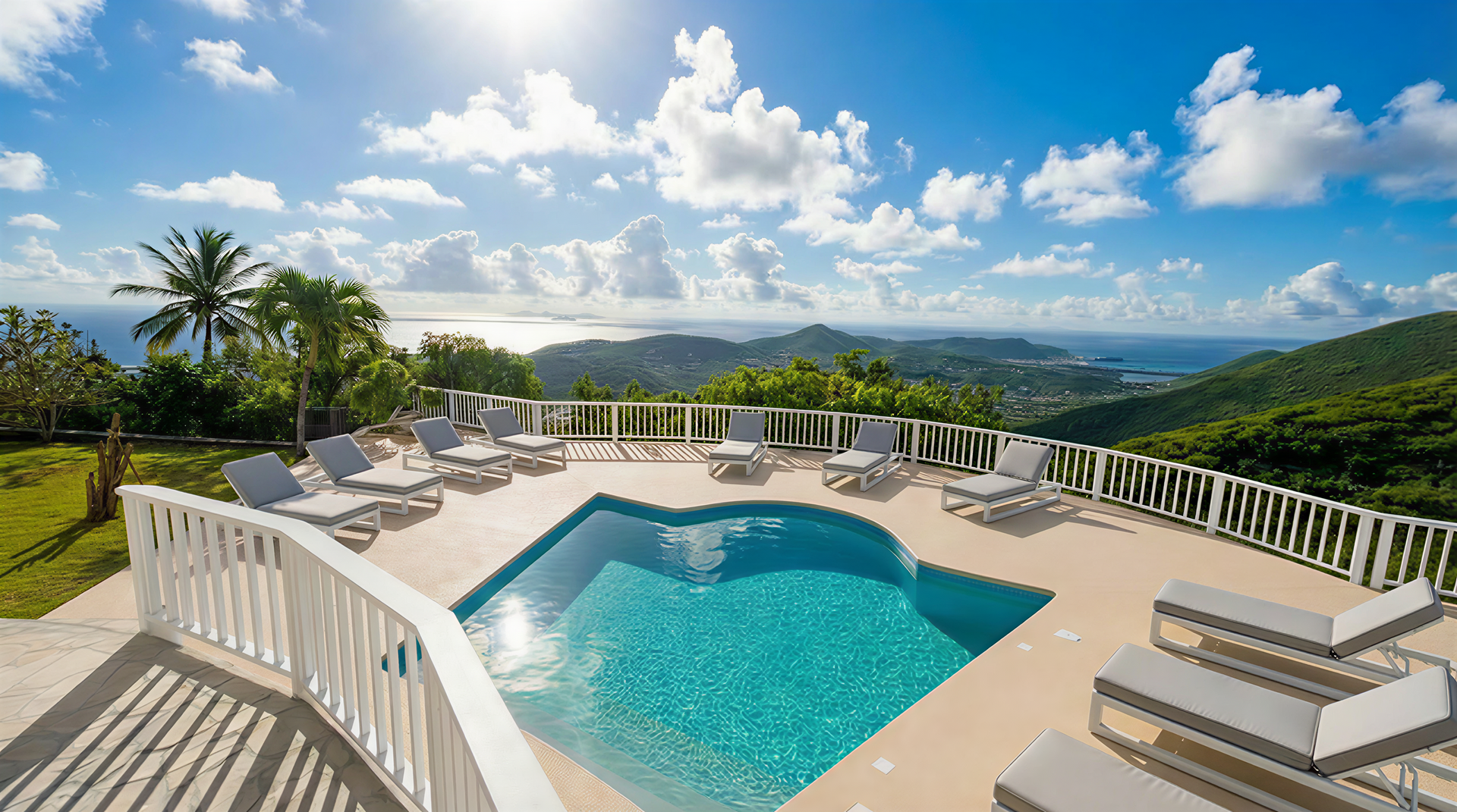 Pool with chaise lounges overlooking lush landscape and ocean, under blue sky with clouds.
