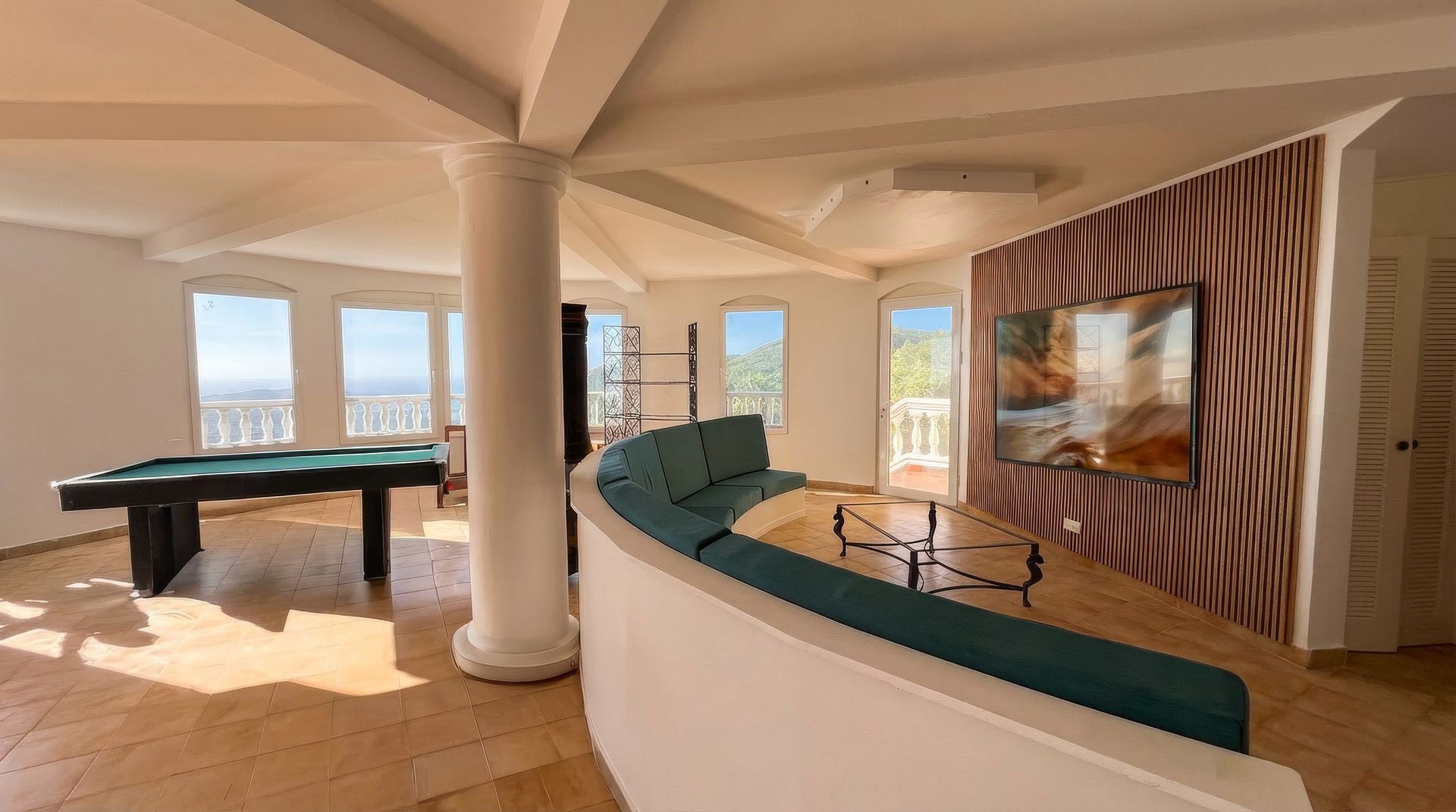 Spacious living area with pool table, curved blue sofa, and large windows with a scenic view.