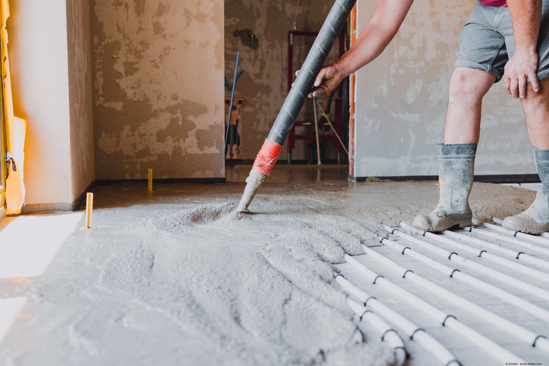 Bauarbeiter verteilt fließfähigen Estrichbeton auf dem Boden in einem Neubau.