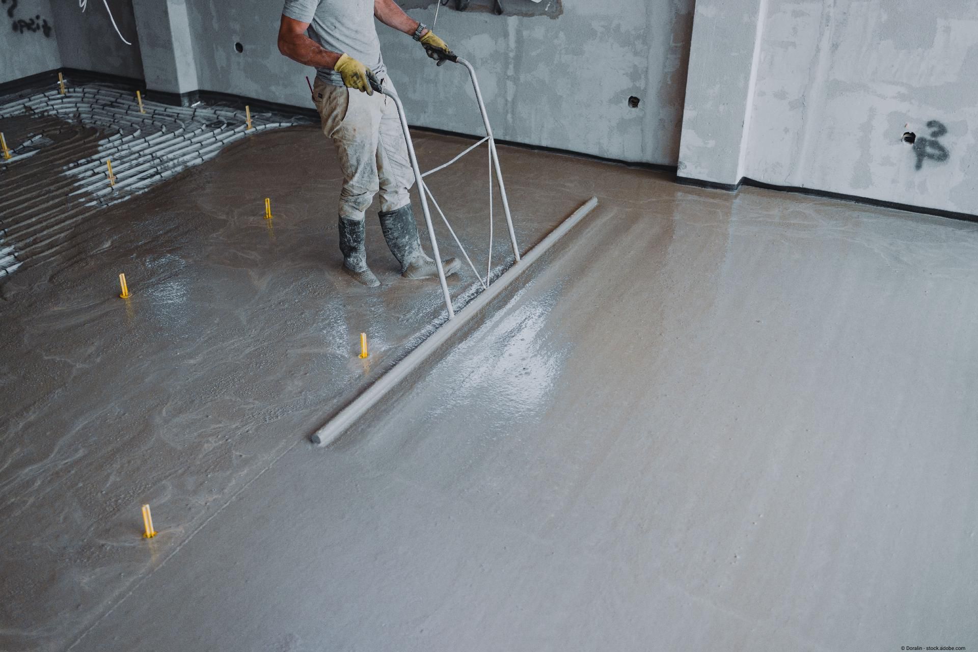 Bauarbeiter glättet frisch gegossenen Betonboden mit einer Abziehlatte.