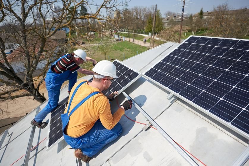 Dos trabajadores con cascos instalando paneles solares en un tejado.