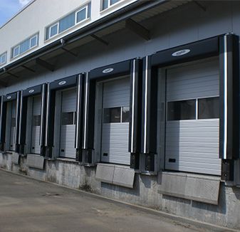 Puertas de muelle en un almacén, con puertas enrollables grises cerradas, marcos negros y paredes de hormigón gris.