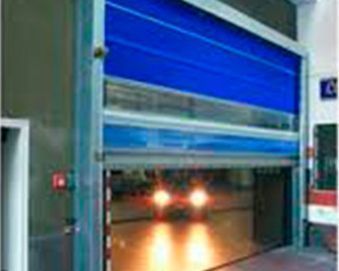 La puerta enrollable de alta velocidad de color azul se abre a un interior luminoso y los faros del coche brillan a través de ella.