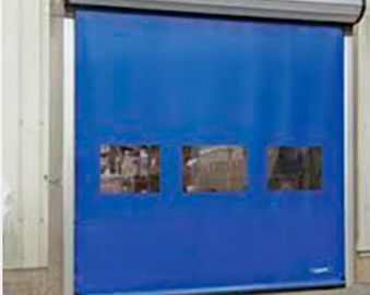 Puerta enrollable industrial azul con tres ventanas rectangulares. La puerta está cerrada y se encuentra en un almacén.