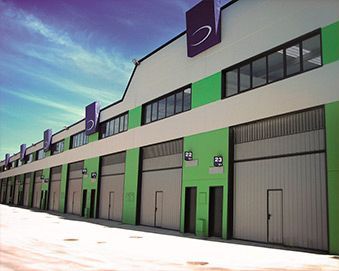 Exterior de un edificio de almacén con detalles en verde claro y varias puertas de muelle de carga, bajo un cielo azul brillante.