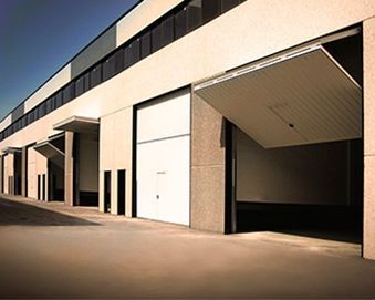 Vista exterior de un edificio comercial con varias puertas grandes blancas, una de ellas parcialmente abierta.