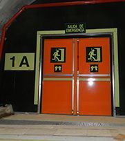 Puertas de salida de emergencia, de color naranja con letreros verdes de persona corriendo, rotuladas