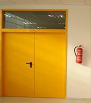 Puertas dobles amarillas con una ventana encima, montadas en una pared blanca con un extintor rojo.
