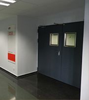 Un pasillo con puertas dobles oscuras, cada una con una ventana. Hay un cartel en la pared izquierda.