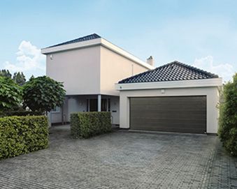 Una casa moderna de dos pisos de color beige con una puerta de garaje gris oscuro y un camino de entrada pavimentado bajo un cielo azul.