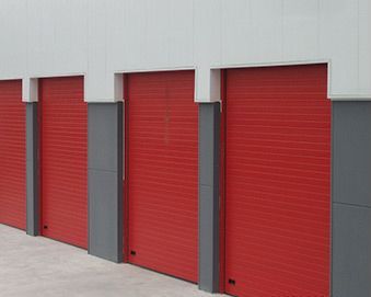 Fila de puertas enrollables rojas en un edificio industrial blanco y gris.