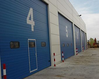 Puertas de garaje azules con las marcas 4, 5 y 6 en un edificio. Están cerradas y hay una pequeña puerta con el número 4.