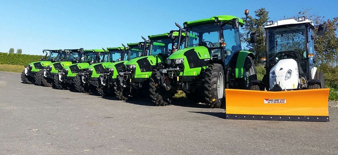 Un tracteur vert laboure un champ au pied d'une montagne aux couleurs d'automne.