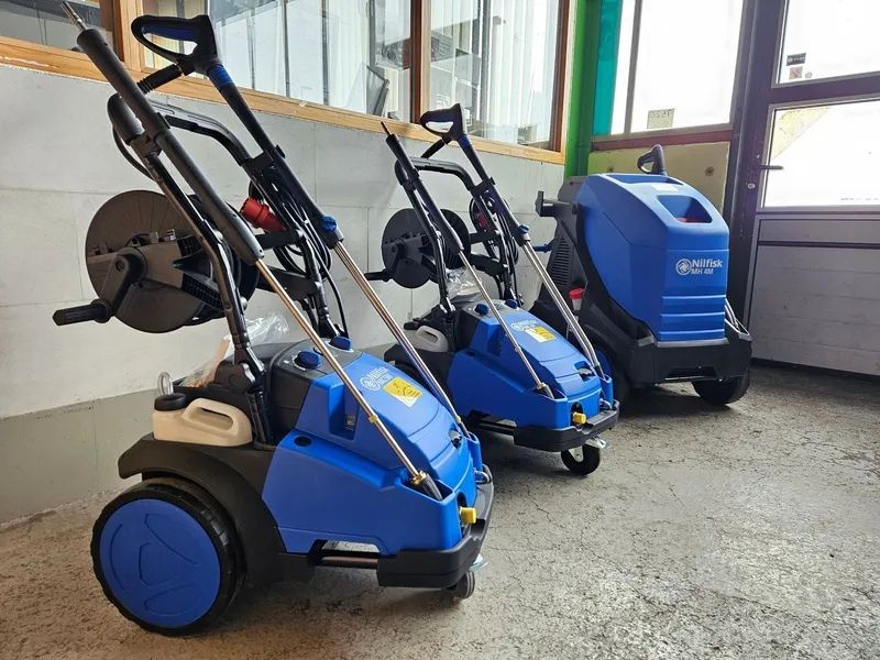 Trois nettoyeurs haute pression bleus dans une pièce bien éclairée. Deux d'entre eux sont équipés d'enrouleurs de tuyau.