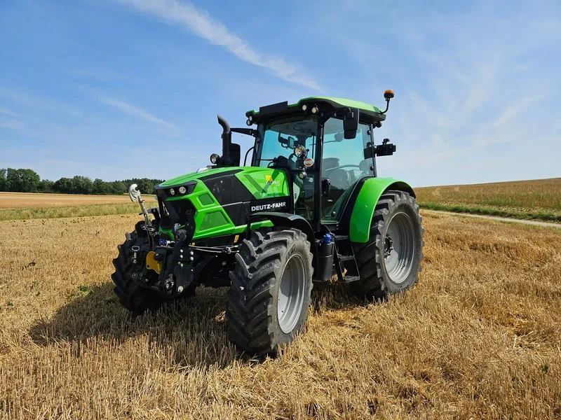Tracteur vert dans un champ moissonné sous un ciel bleu.
