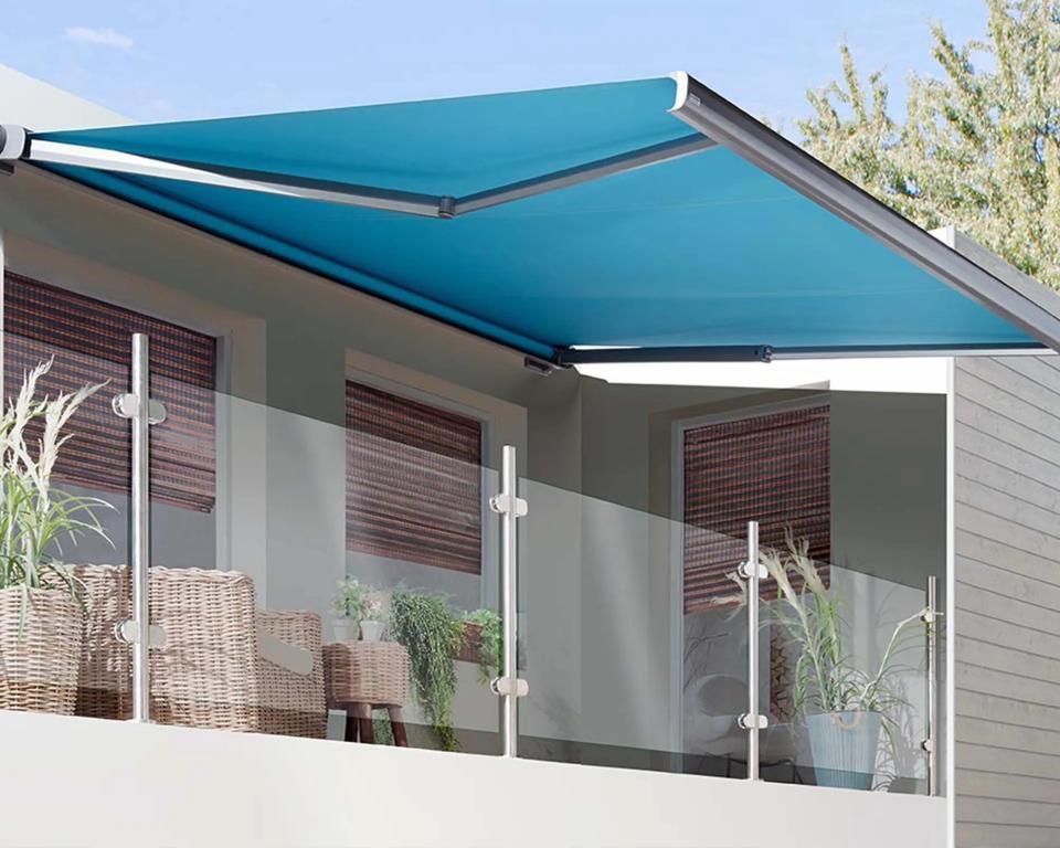 Eine leuchtend blaue, ausfahrbare Markise über einem modernen Balkon mit Glasgeländer und Topfpflanzen.