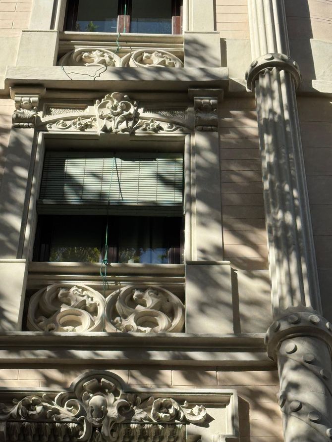 Tallas de piedra en la fachada de un edificio. Piedra beige con detalles intrincados y una persiana cerrada.