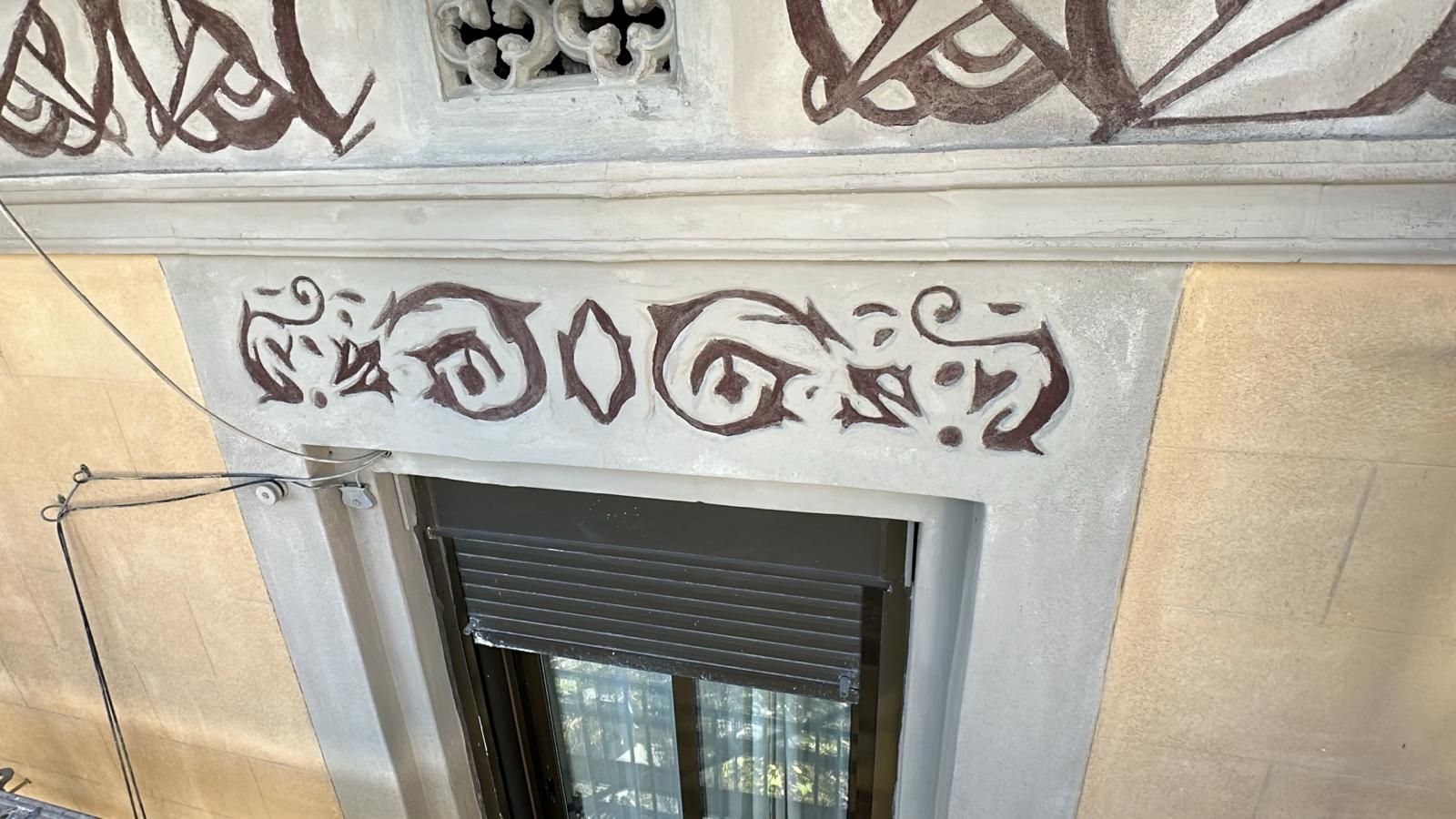 Exterior del edificio con ornamentación marrón sobre una ventana con contraventana enrollable oscura cerrada.