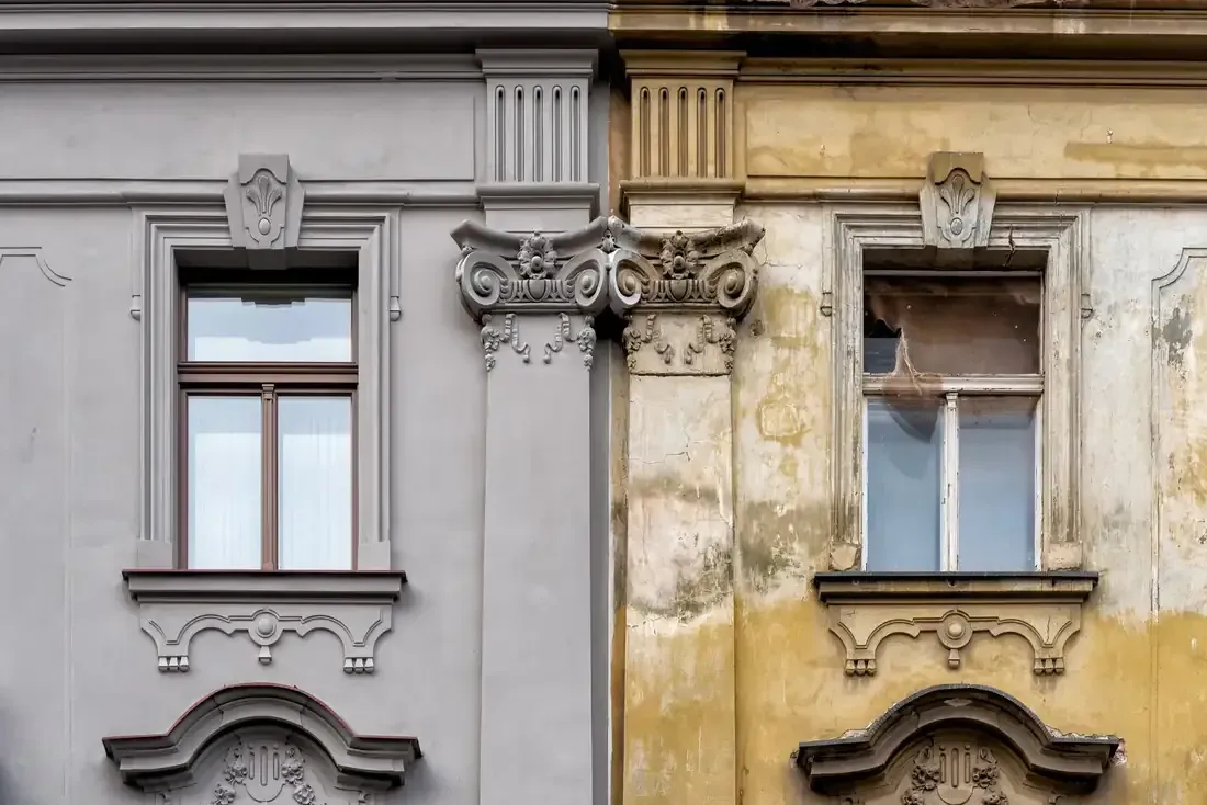 Dos fachadas de edificios adyacentes, una gris y otra amarilla, con marcos de ventanas decorativos y detalles ornamentales.
