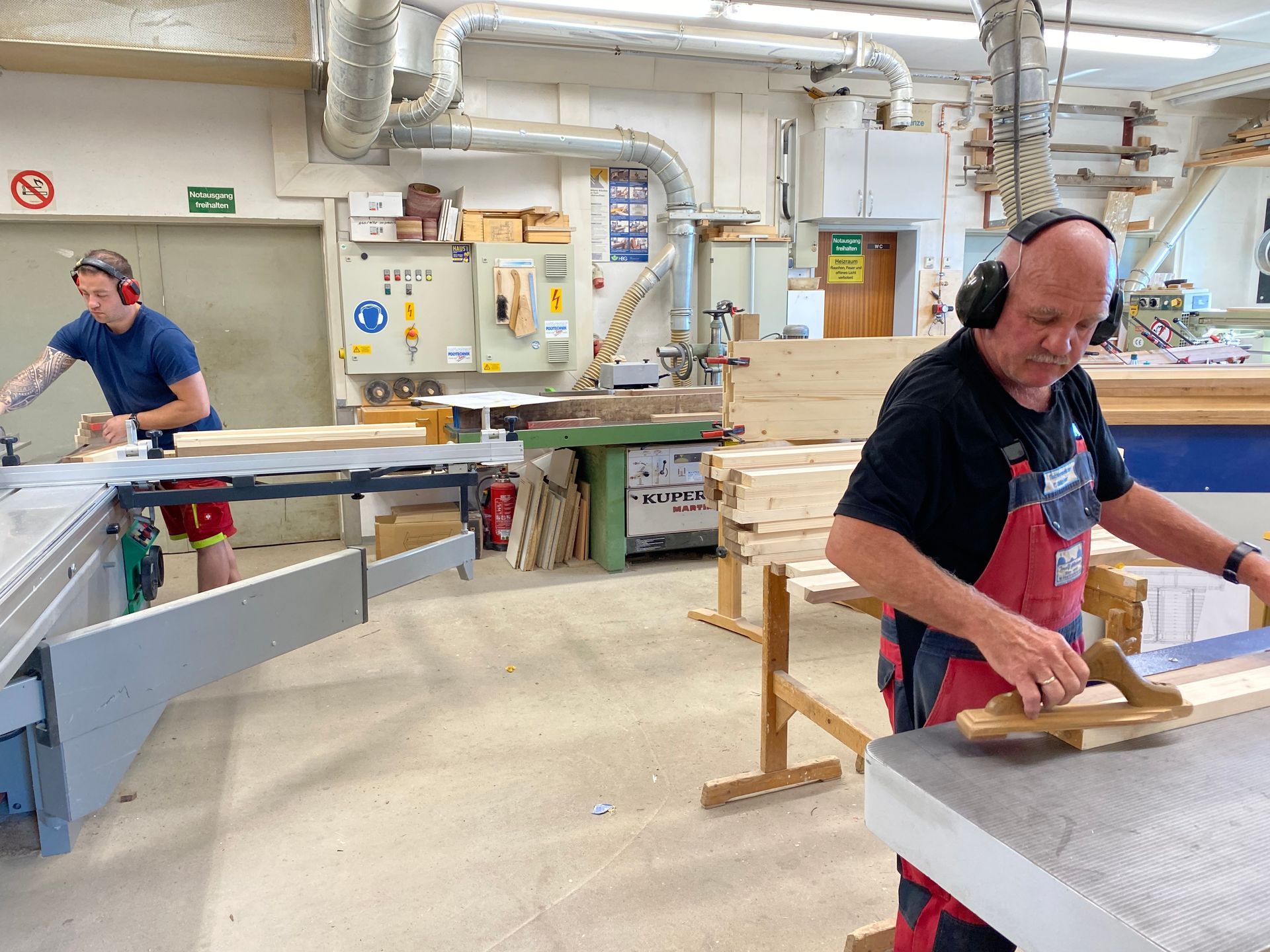 Ein Mann mit Hut und hellen Hosen dichtet ein Fenster ab, die Außenseite eines Gebäudes ist sichtbar.