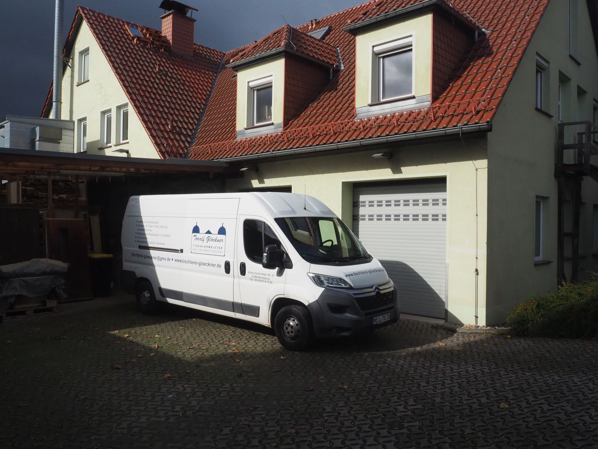 Mann streicht im Innenbereich eine Holzkonstruktion, trägt Handschuhe und Brille.