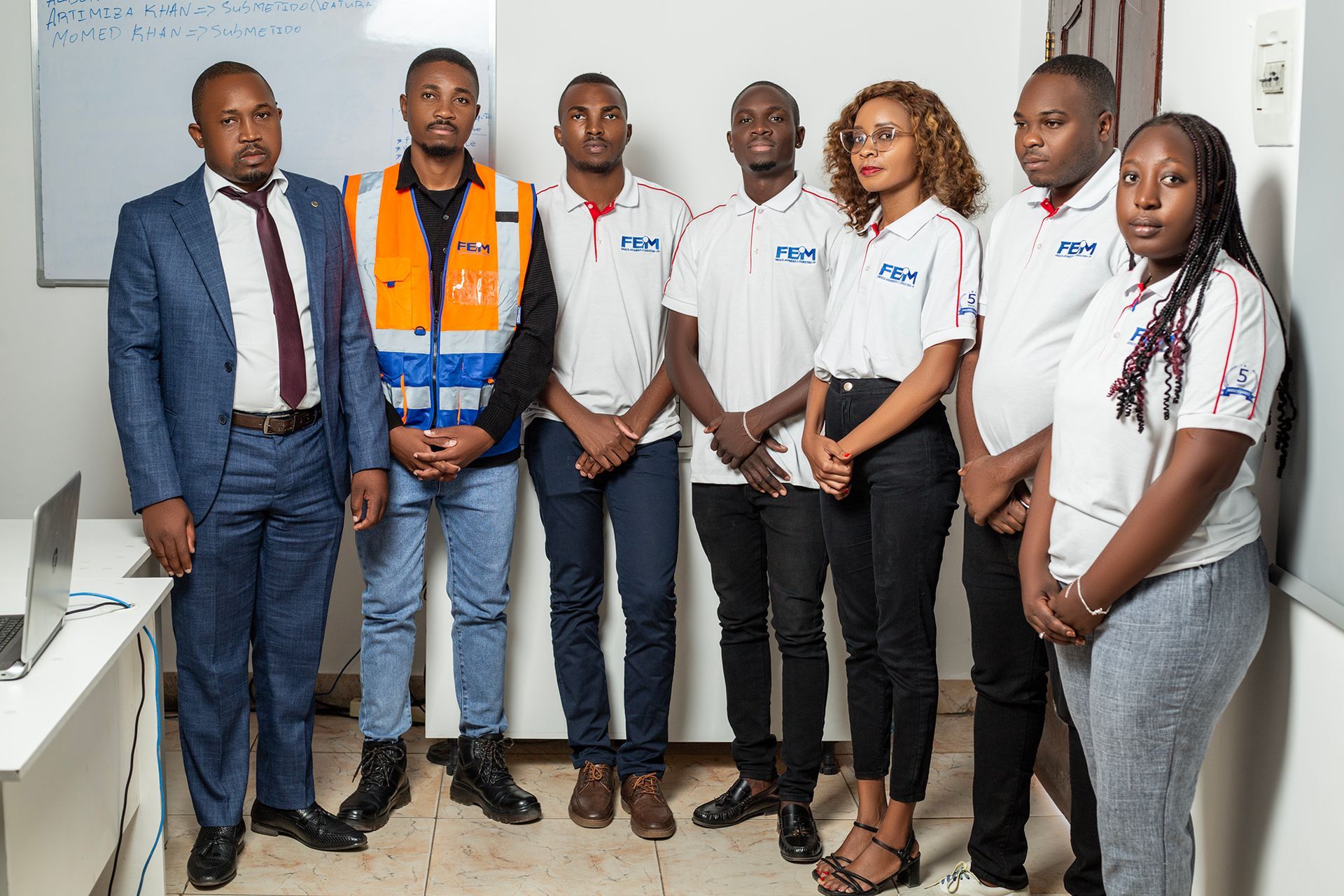Group of people in a room, some wearing company shirts. One person in a safety vest.