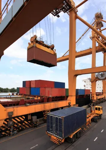 Cargo containers being loaded onto trucks at a port by a large orange crane.