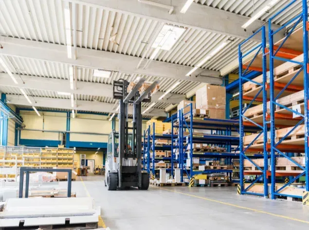 Forklift in a warehouse, picking up items from a rack. The warehouse has shelves and bright lighting.