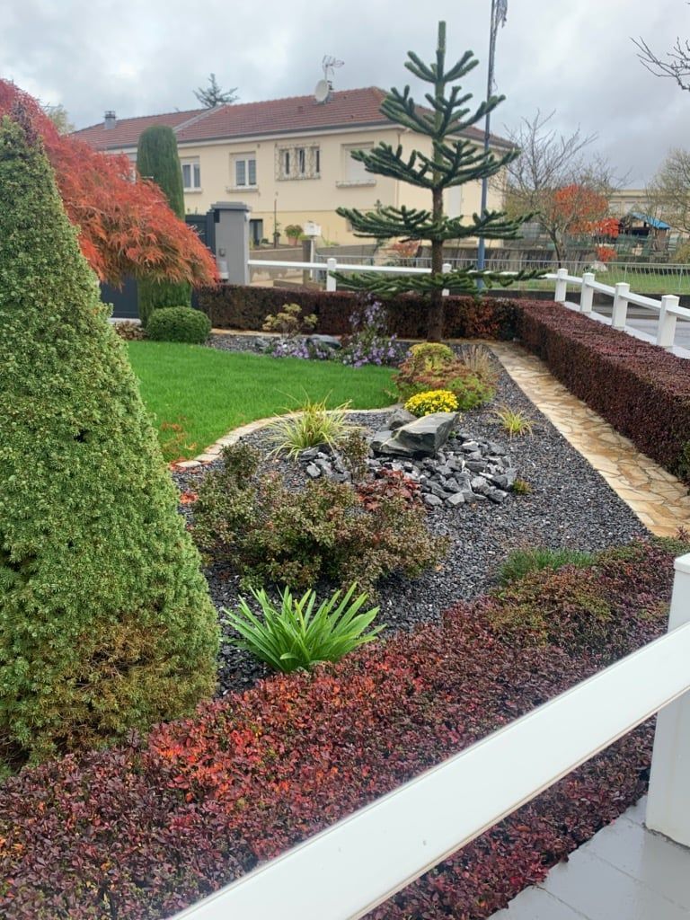 Cour de jardin pluvieuse avec arbustes taillés, couvre-sol rouge et une maison en arrière-plan