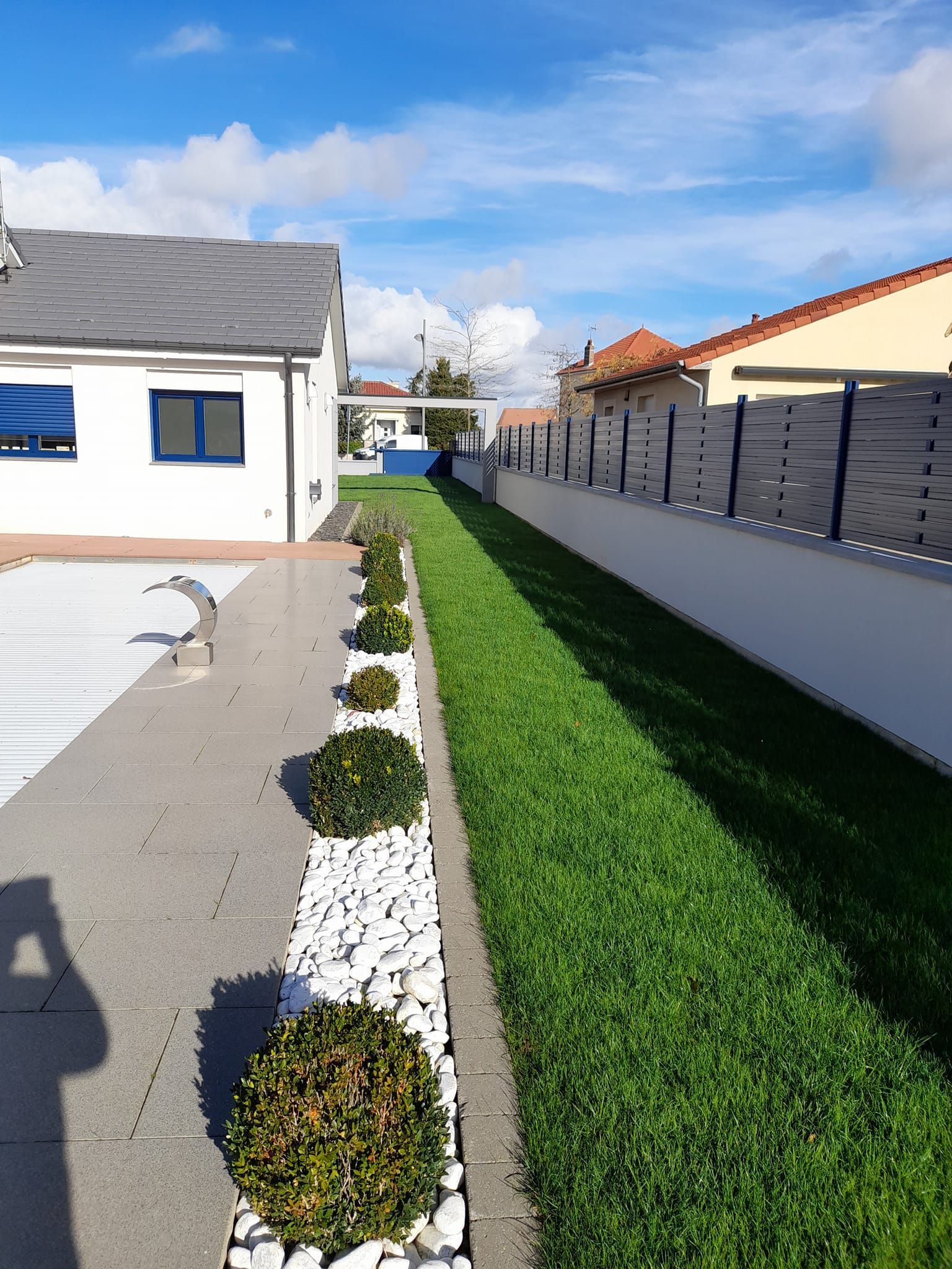 Pelouse bien tondue autour d'une piscine entourée de massifs en galets blancs