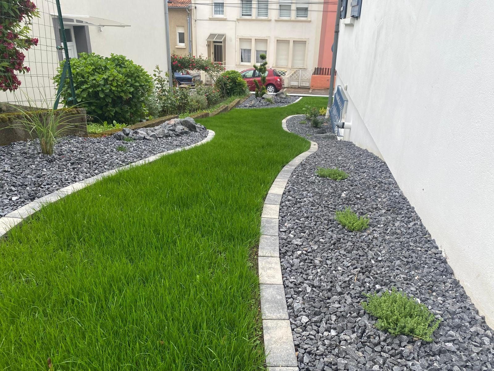 Allée sinueuse en pelouse verte bordée de pierres grises dans une petite cour paysagée