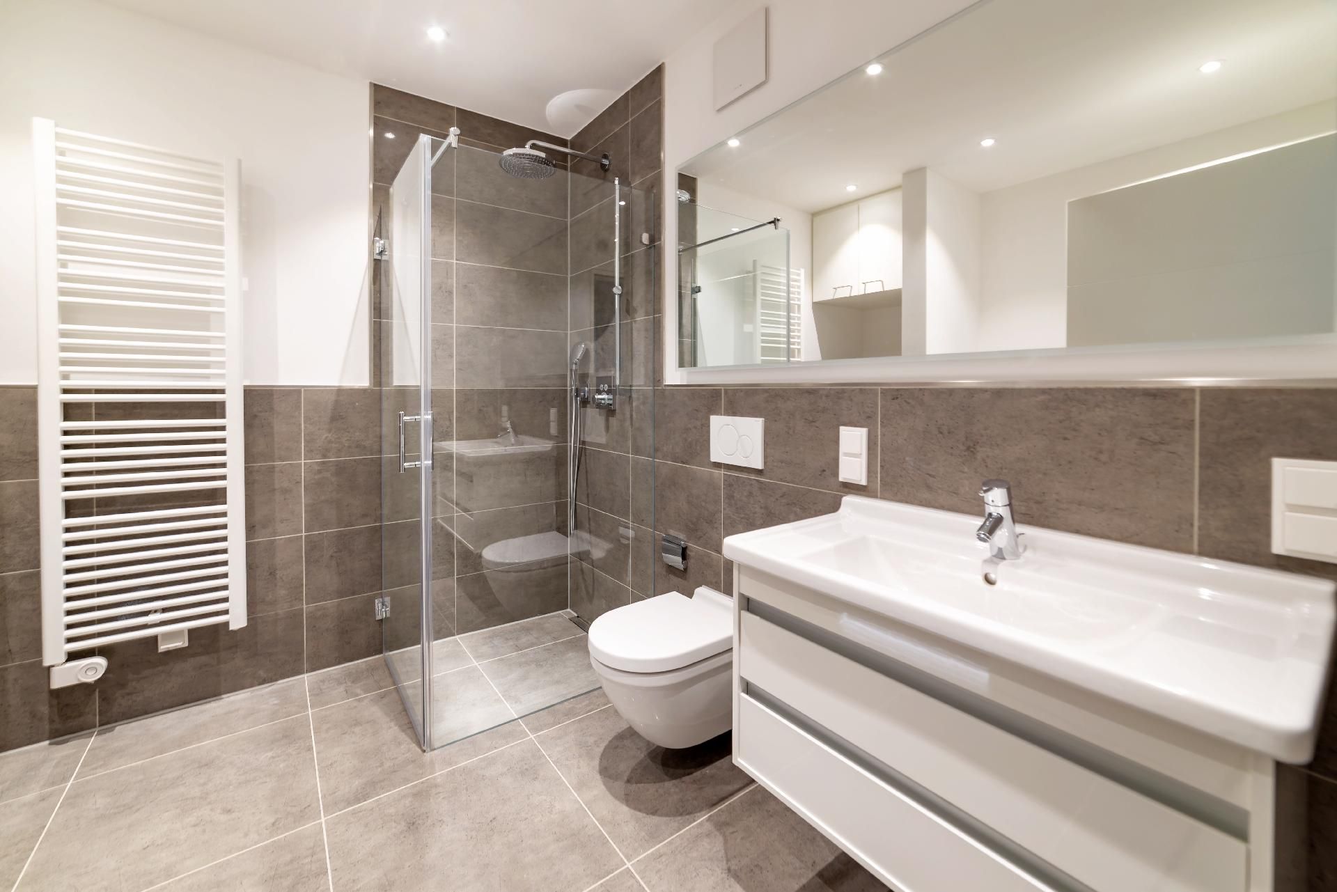 Modernes Badezimmer mit grau gefliesten Wänden, einer begehbaren Glasdusche, wandhängendem WC und Waschtisch